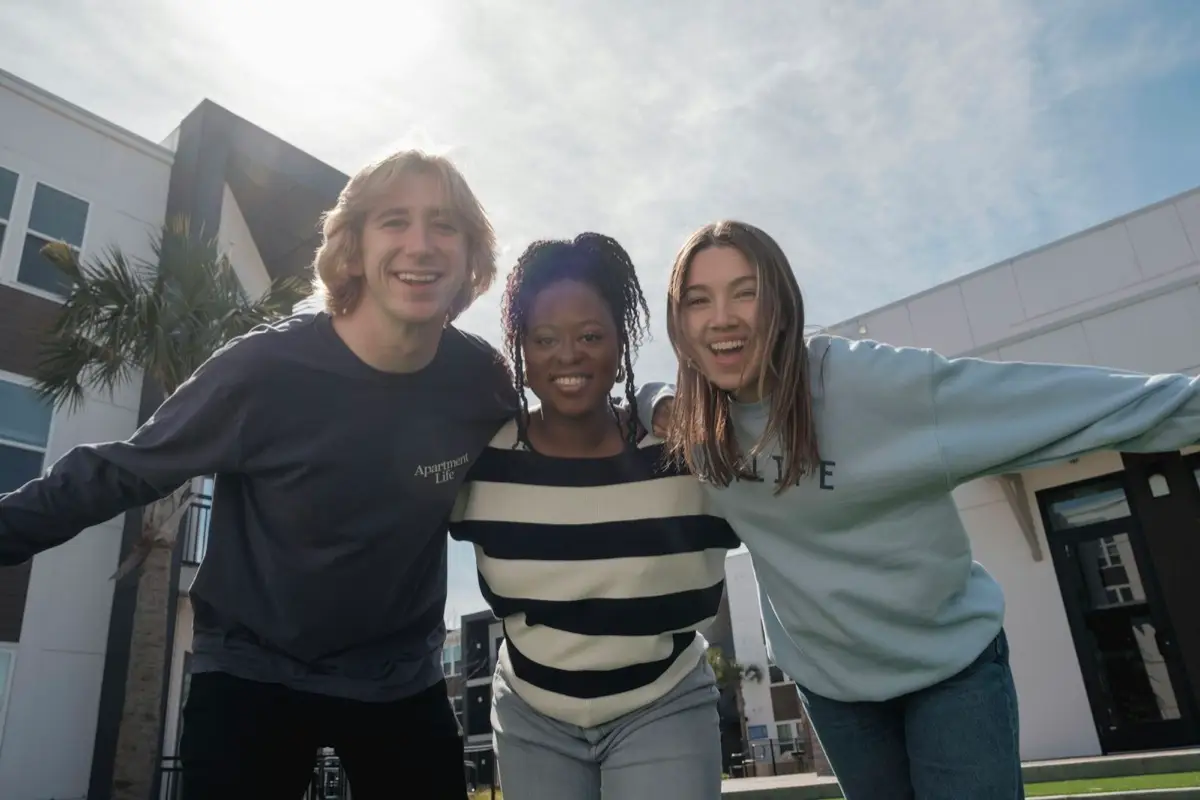 Three friends standing close together with arms around each other, smiling